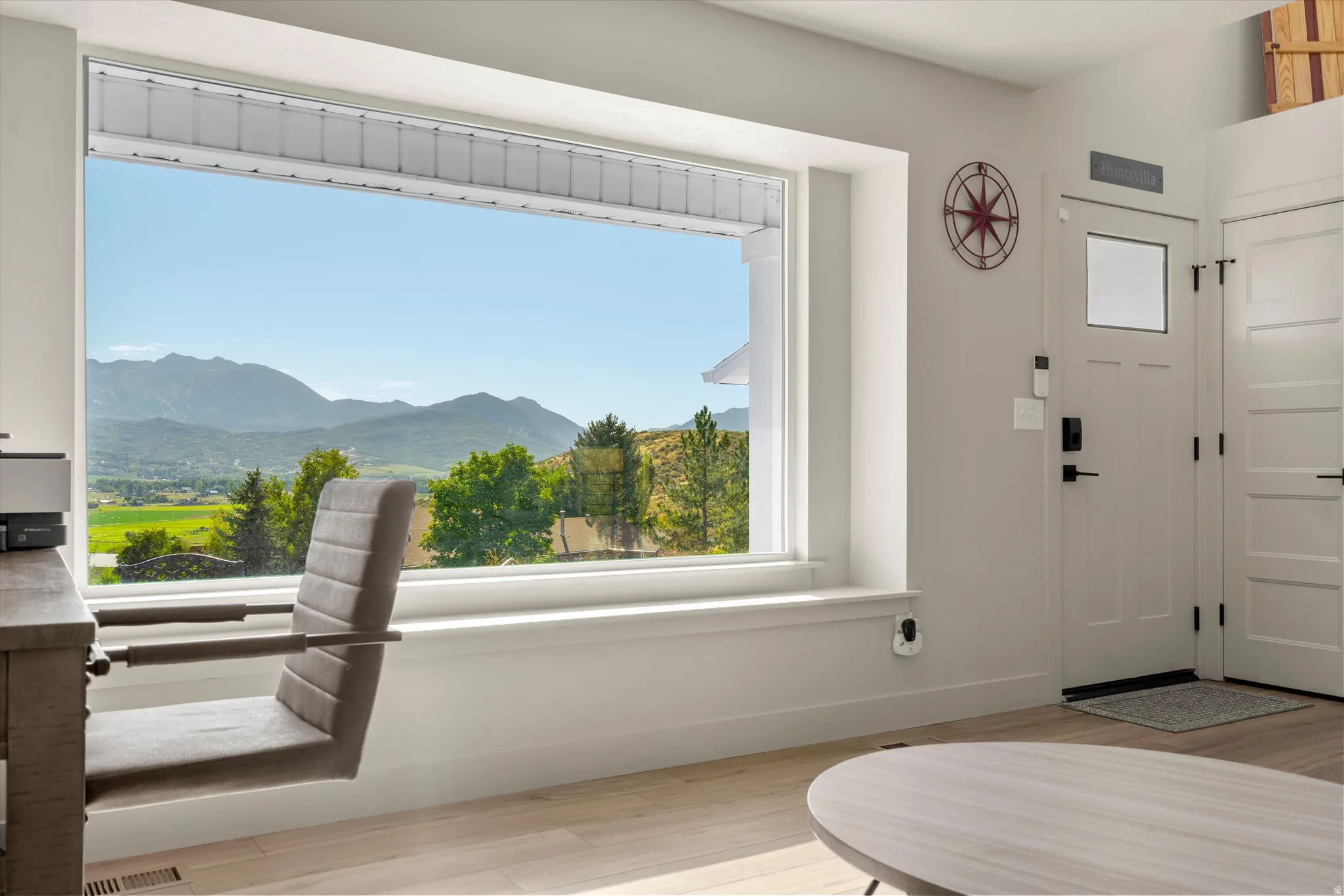Expansive window with mountain scenery, light wood-finish flooring, white panel door, and white trim