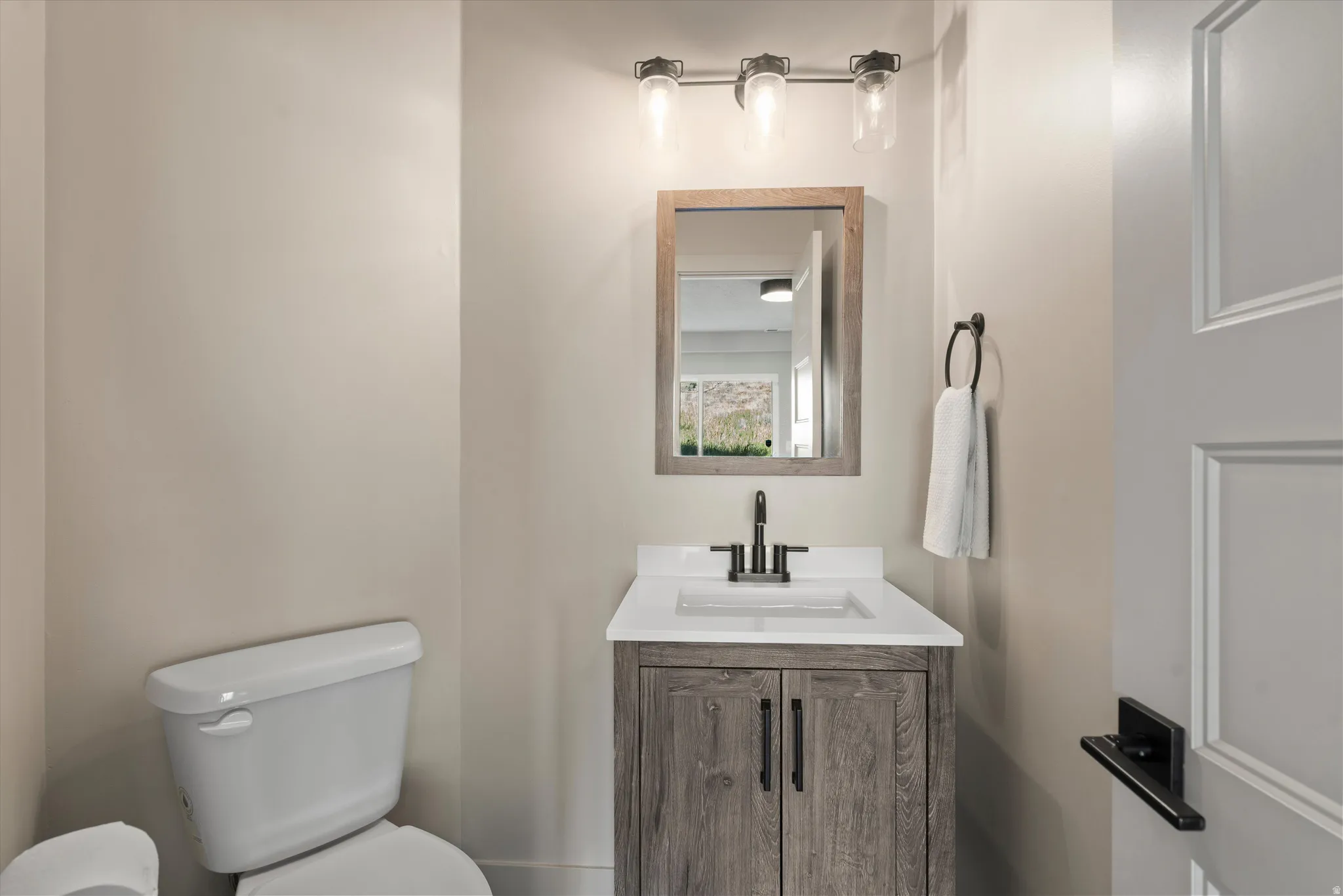 Powder room featuring a wood-finish vanity with a white countertop and undermount sink, matte black hardware, and a three-light vanity fixture