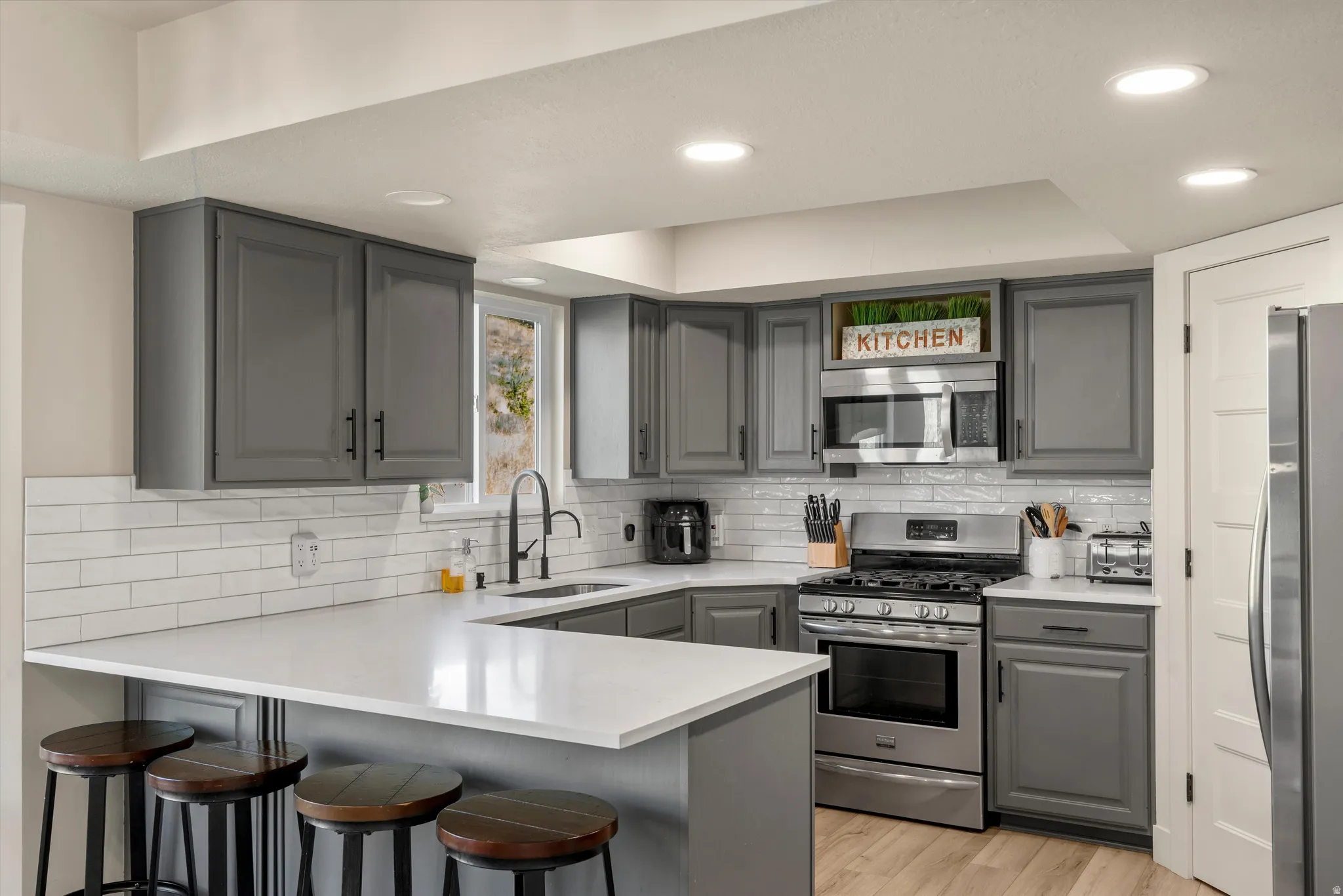 Kitchen featuring gray cabinetry with black hardware, white subway tile backsplash, white countertops, and stainless steel appliances