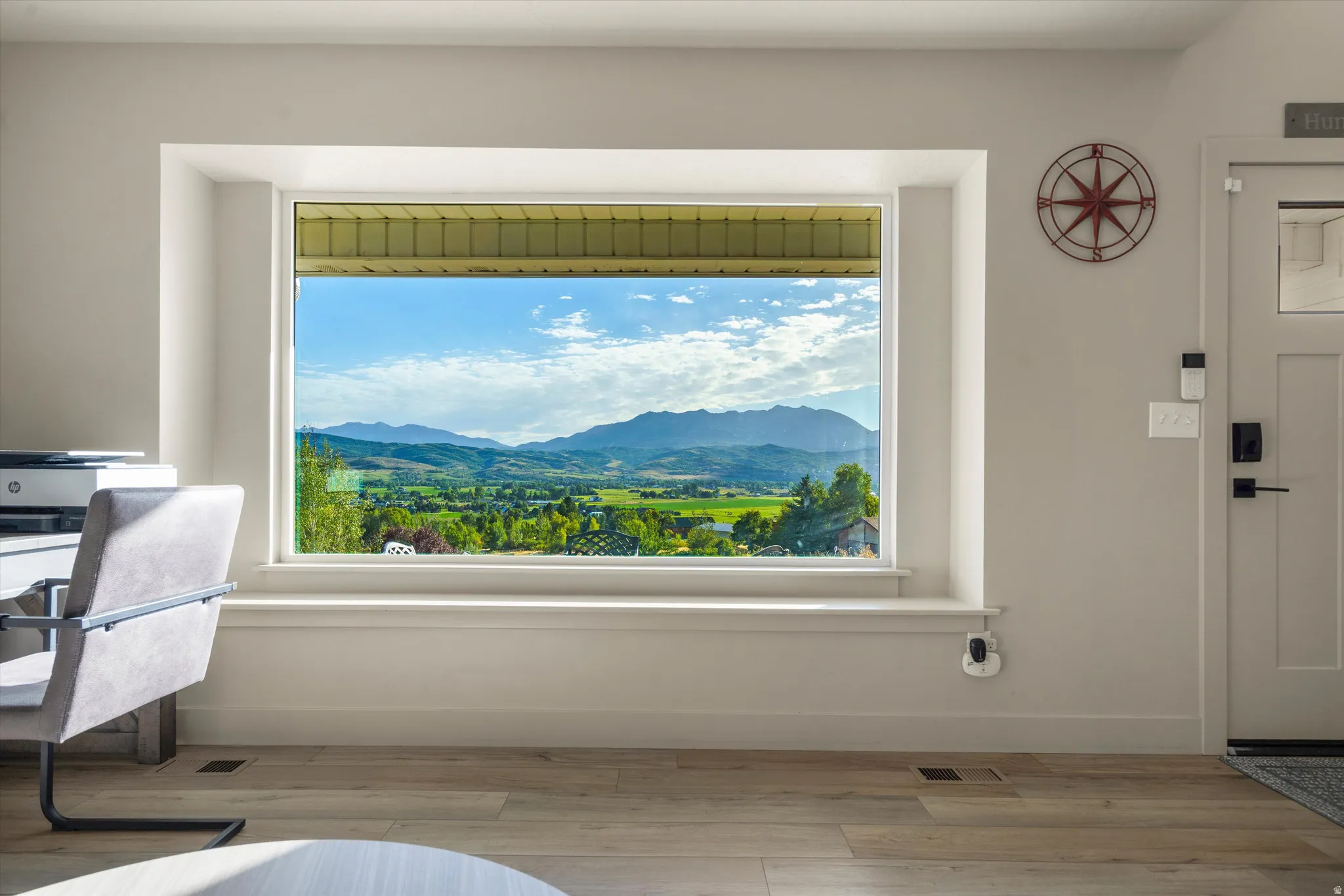 Expansive window with mountain and valley scenery, wide window sill, light wood-finish flooring, and a paneled entry door with black hardware