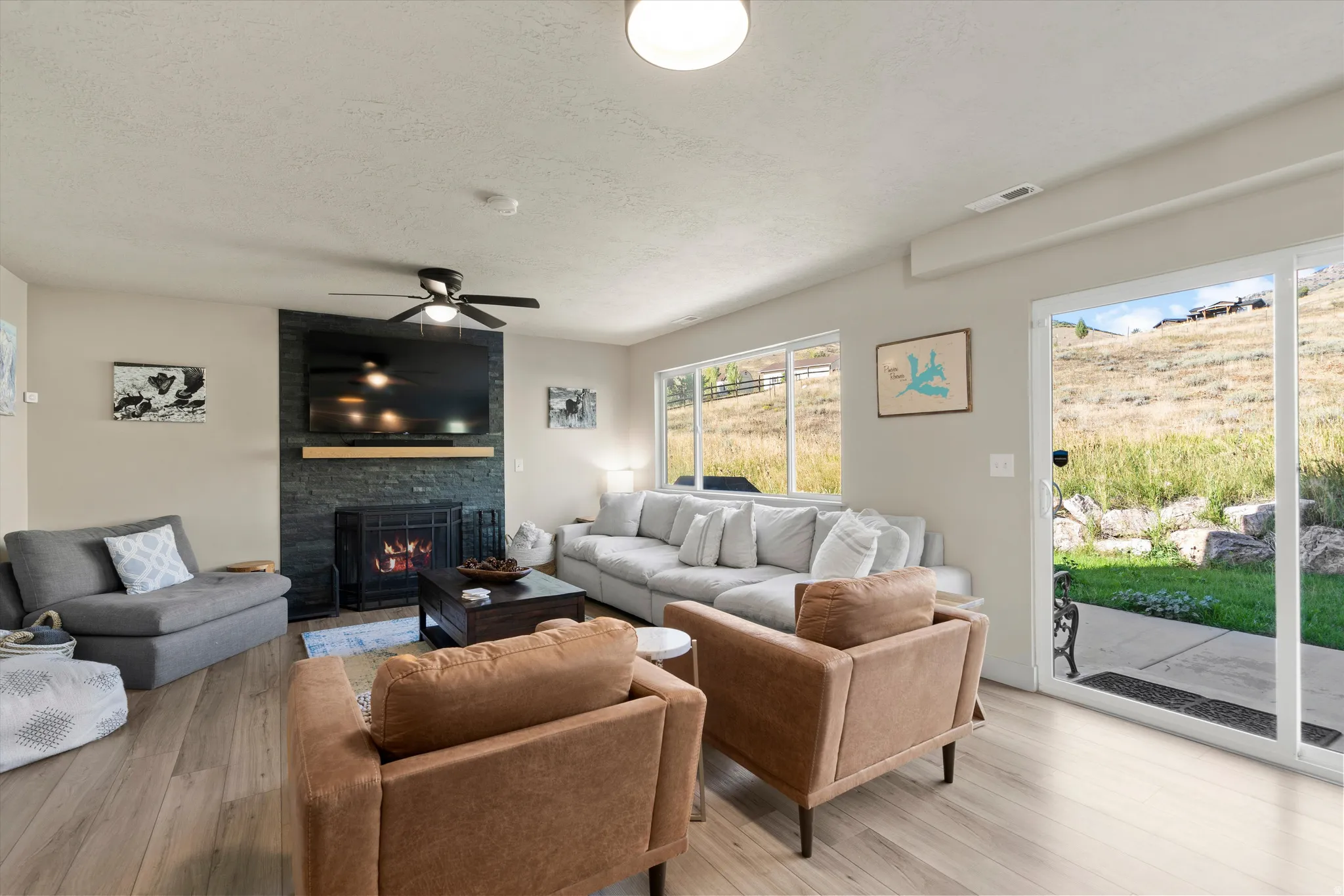 Open-concept living space featuring wood-finish flooring, a contemporary fireplace with a stone surround, and a ceiling fan