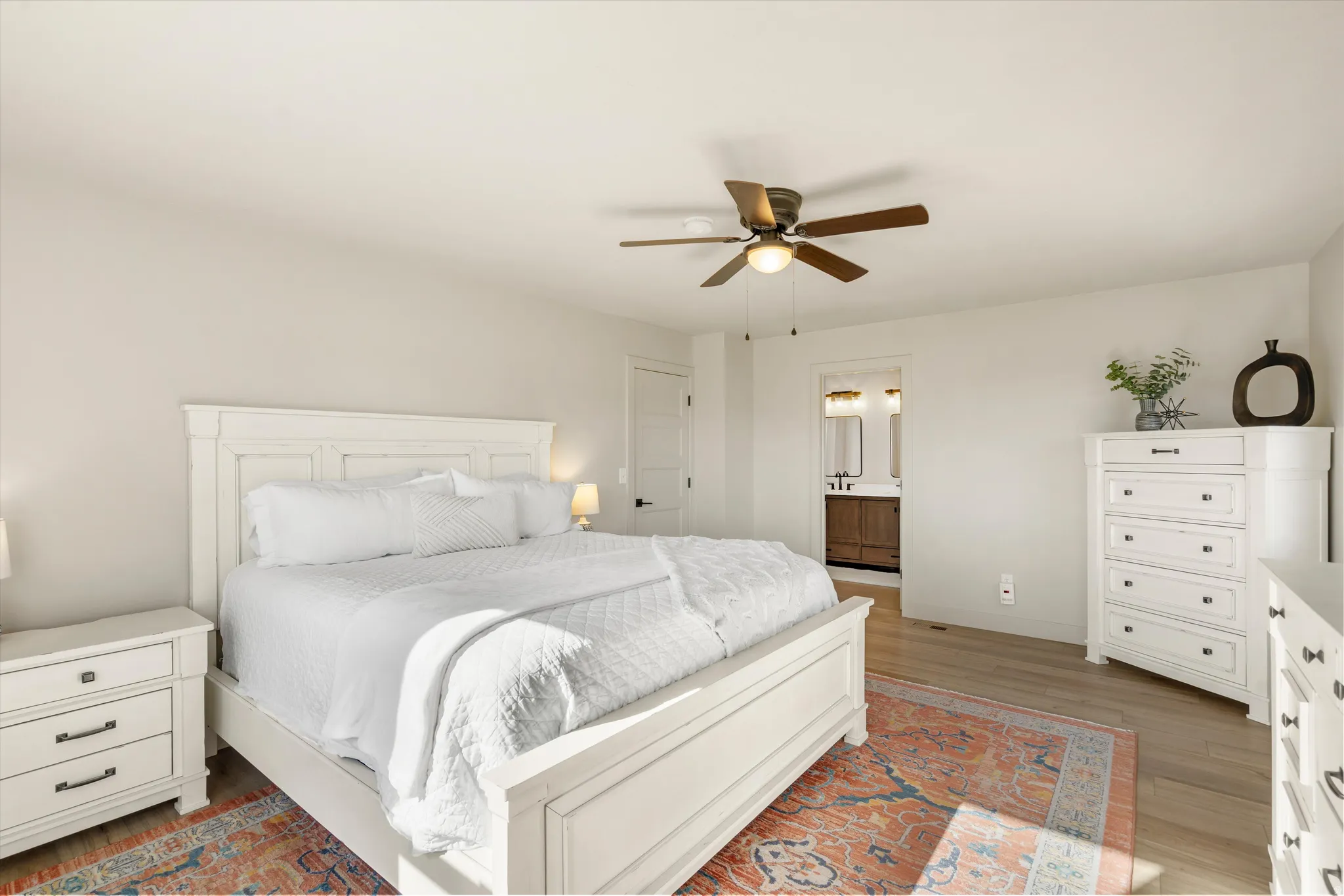 Recessed lighting, ceiling fan with integrated light, wood-finish flooring, white painted walls, and a visible doorway to a bathroom with dual vanity