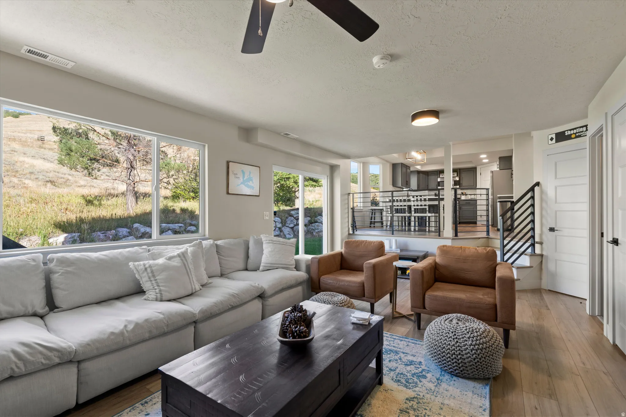 Open-concept living area with large picture windows, wood-finish flooring, and a ceiling fan