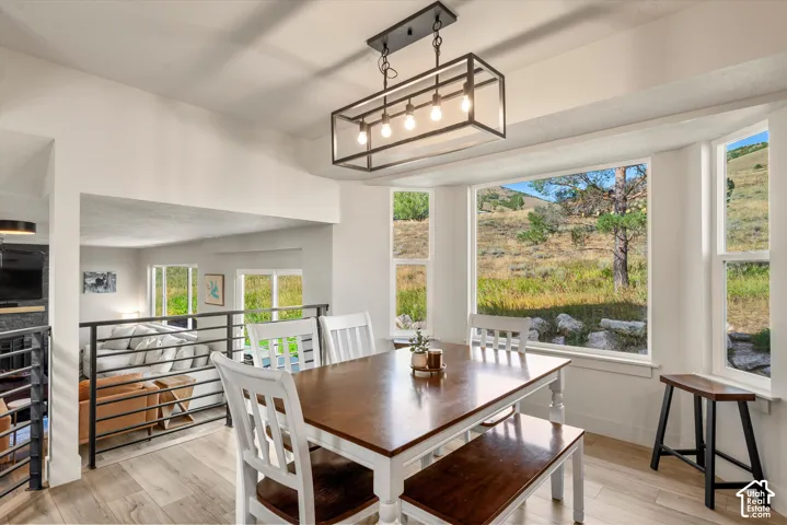 Open-concept dining area featuring wood-finish flooring, a contemporary linear chandelier, expansive bay windows, and a metal railing overlooking a lower level