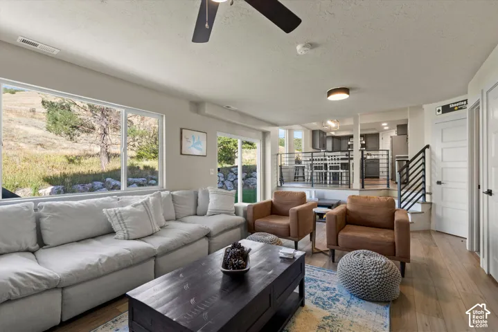 Open-concept living area with large picture windows, wood-finish flooring, and a ceiling fan