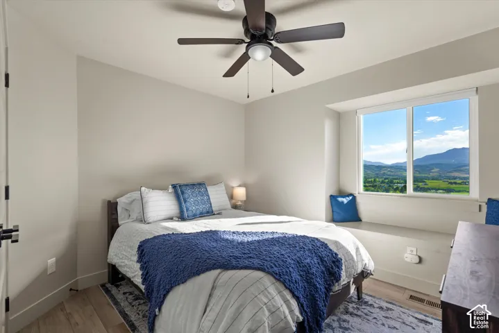 Light wall color, window seat, mountain scenery, wood-finish flooring, and ceiling fan