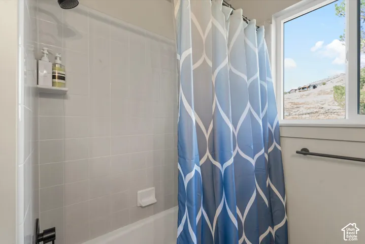 Tub and shower combination featuring light gray tile surround, matte black shower head, and a window providing natural illumination