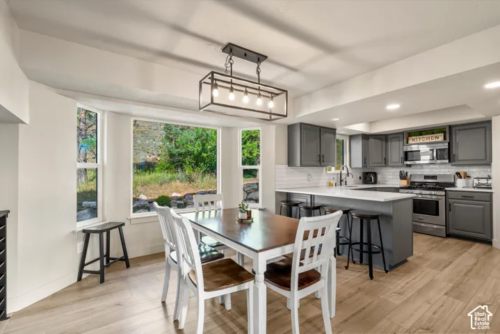 Kitchen with grey cabinetry, stainless steel appliances, white subway tile backsplash, and light wood-finish flooring