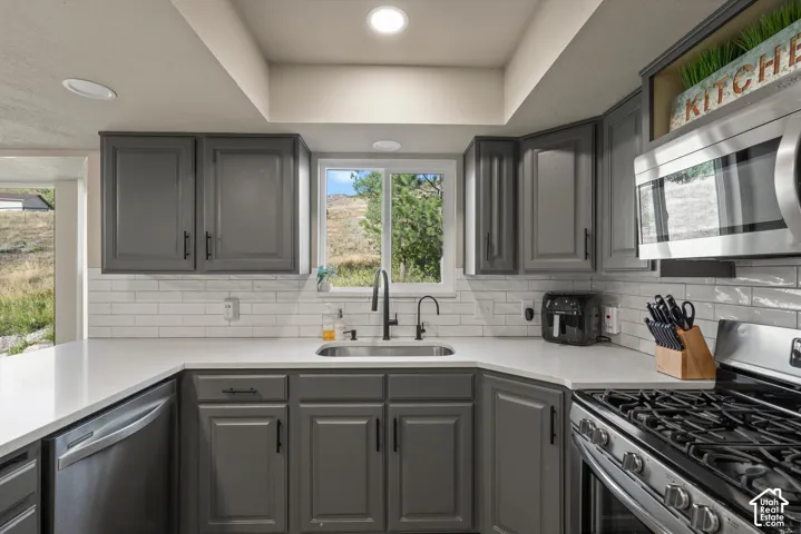 Kitchen featuring grey shaker-style cabinetry, white subway tile backsplash, white countertops, stainless steel appliances, and a stainless steel sink with a matte black faucet