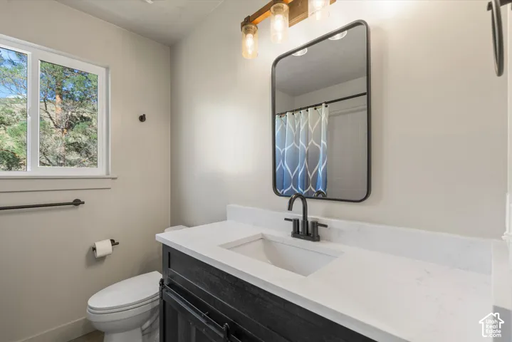 White-framed window, vanity with a white countertop, undermount sink, and black faucet, rectangular wall mirror with a black frame, and a three-light vanity fixture
