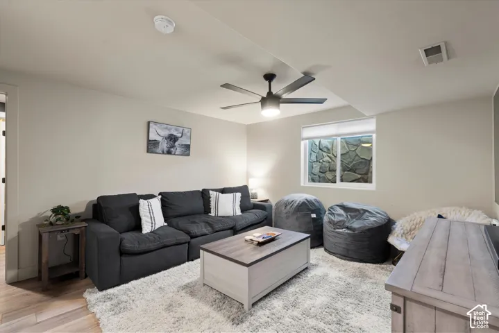 Recessed lighting, ceiling fan with integrated light, wood-finish flooring, and a stone-lined window well
