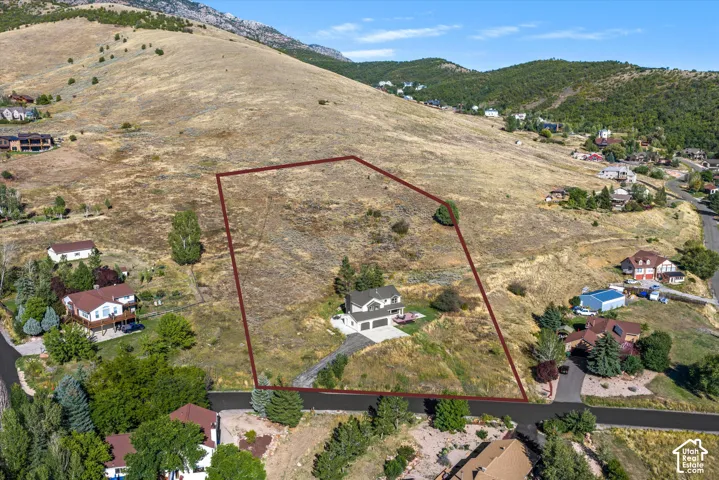 Expansive sloped lot bordered by paved roadways and mature trees, featuring a two-story residence with an attached two-car garage