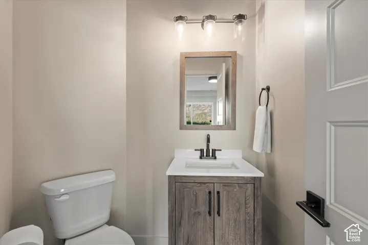 Powder room featuring a wood-finish vanity with a white countertop and undermount sink, matte black hardware, and a three-light vanity fixture