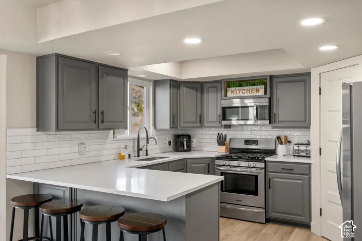 Kitchen featuring gray cabinetry with black hardware, white subway tile backsplash, white countertops, and stainless steel appliances