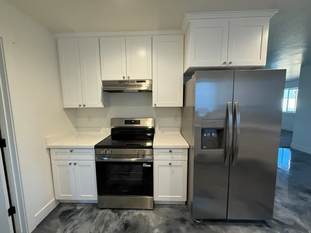Kitchen featuring white shaker cabinetry, stainless steel appliances, light-toned countertops, and a range hood