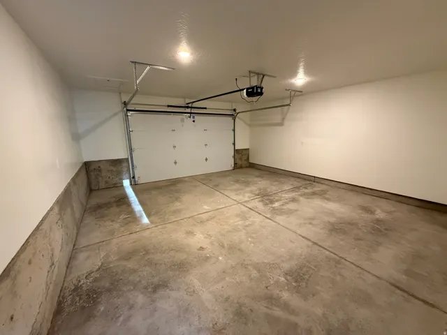 Attached garage featuring a sectional overhead door, concrete flooring, painted walls, and ceiling-mounted lighting