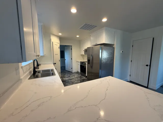 Kitchen featuring white cabinetry, light-toned countertops, a stainless steel double basin sink with a matte black faucet, and recessed lighting