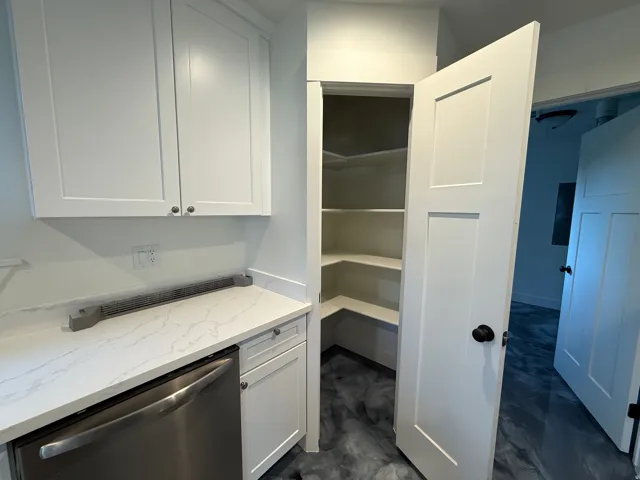 White shaker-style cabinetry with brushed nickel hardware, white quartz countertops with subtle veining, stainless steel dishwasher, and a corner pantry with built-in shelving