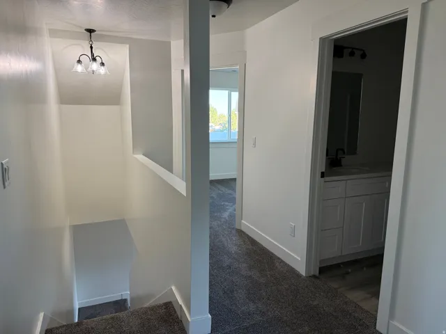 Plush carpeted flooring, a contemporary chandelier, a white vanity with a dark countertop, and modern lighting fixtures