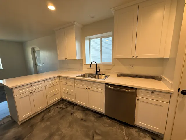 Modern kitchen featuring white shaker cabinetry, an L-shaped countertop, stainless steel sink with a matte black faucet, and a stainless steel dishwasher