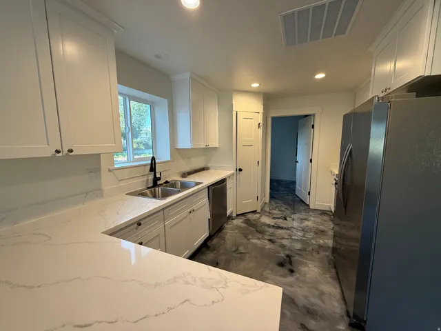 White shaker cabinetry, light-toned countertops, double basin sink with a matte black faucet, integrated dishwasher, and stainless steel refrigerator