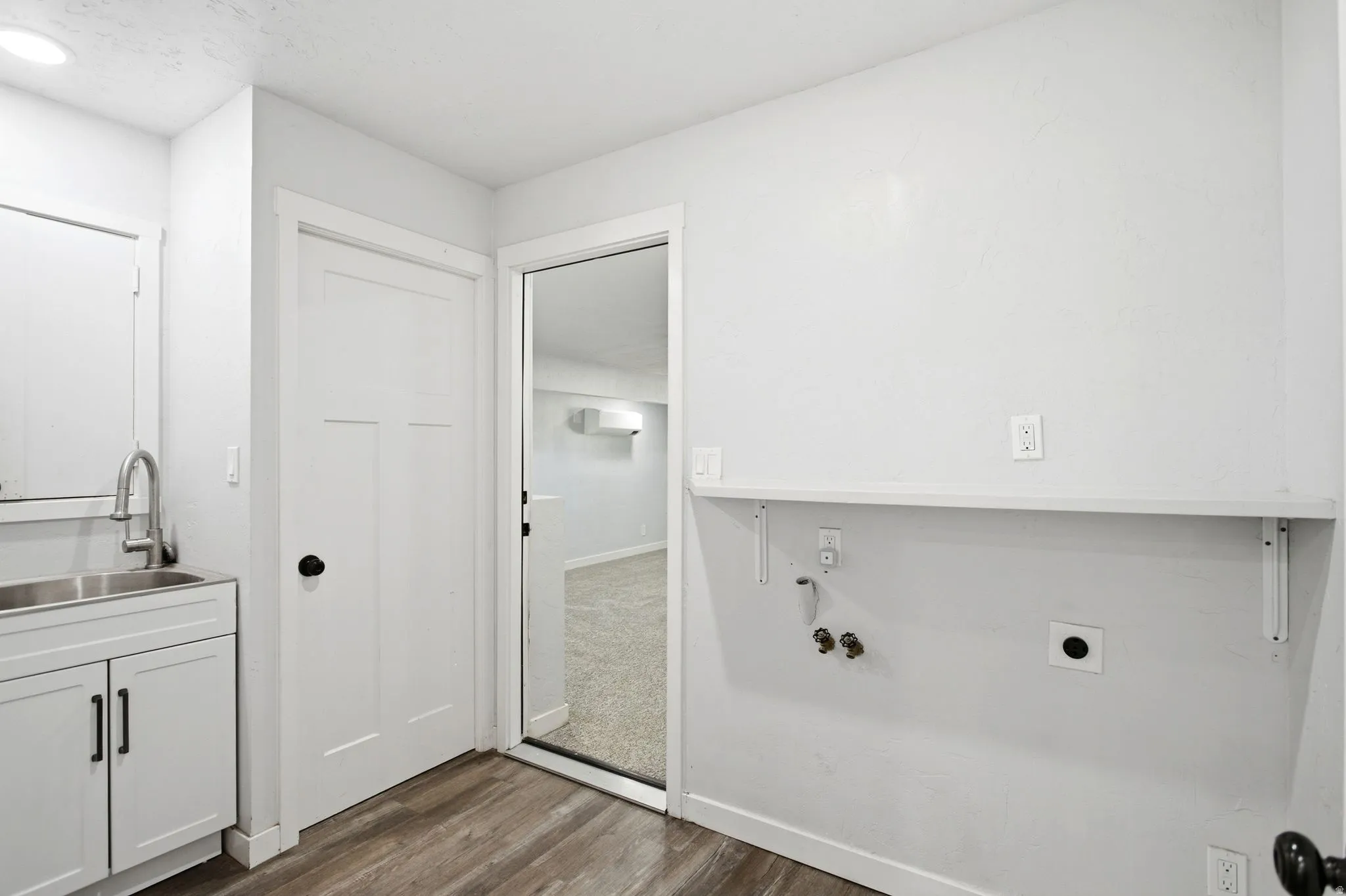 Wood-finish flooring, white cabinetry with matte black hardware, stainless steel sink with gooseneck faucet, white interior doors, and a built-in wall shelf