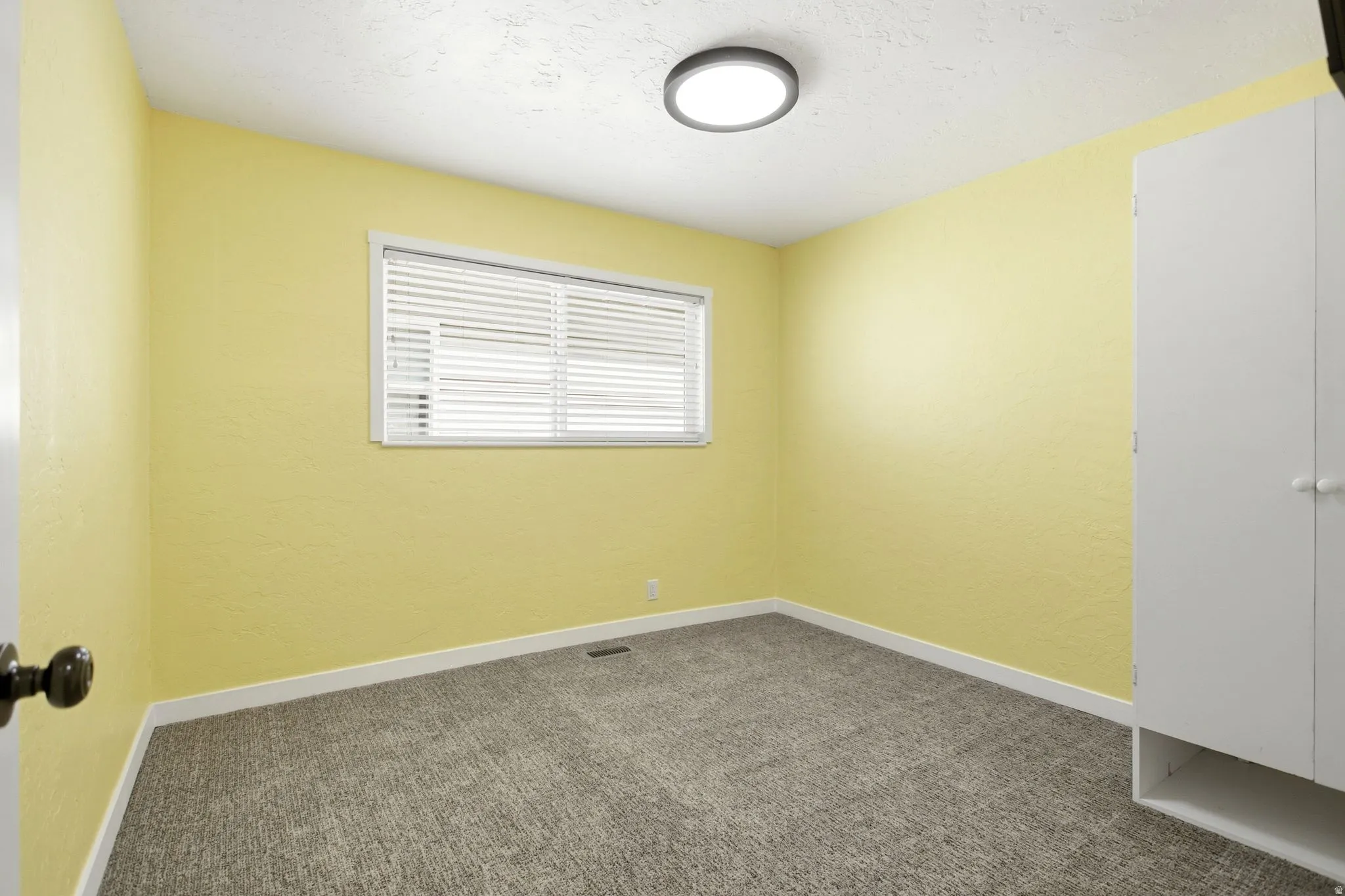 Textured walls, grey carpet flooring, white trim, window with blinds, and a built-in closet with white doors