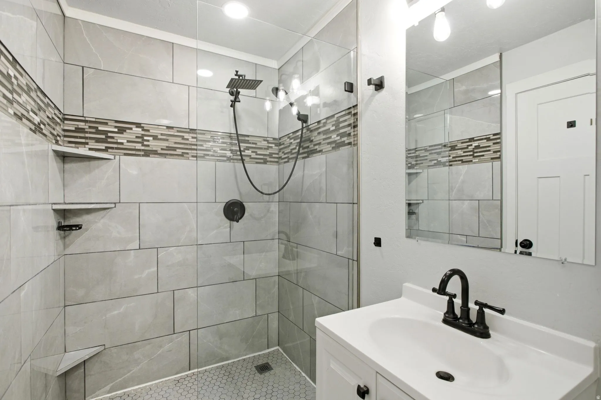 Master bathroom with shower with glass enclosure, tiled walls featuring a decorative mosaic band, and built-in corner shelves