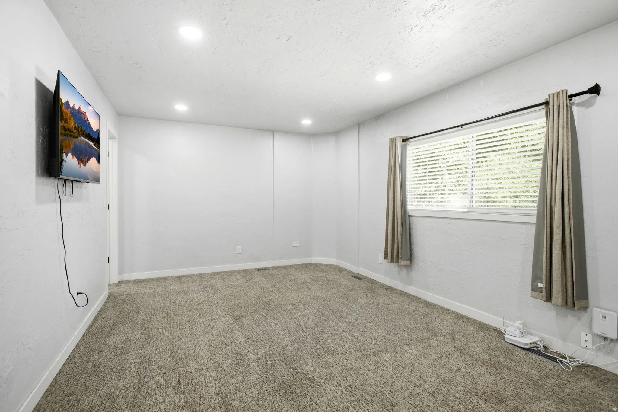 Master bedroom with recessed lighting illuminates the room, featuring a window with horizontal blinds and a privacy curtain rod