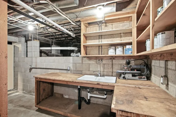 Utility area featuring a sink, wood-finish countertops, built-in shelving, concrete block walls, and exposed overhead piping