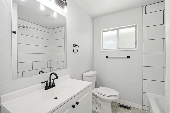 White vanity with integrated sink, black fixtures, subway tile shower surround, and a frosted window