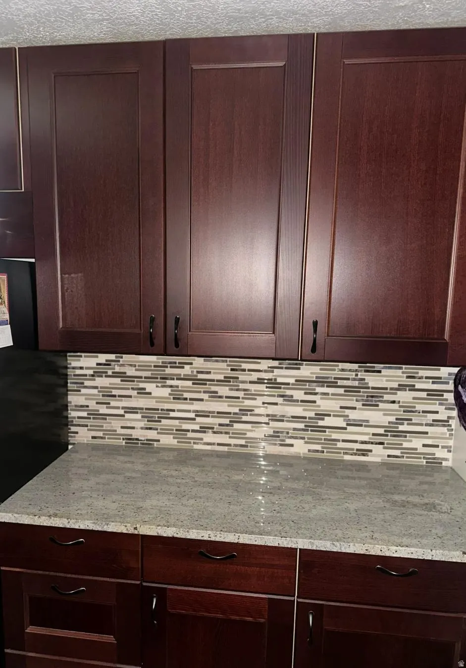 Dark wood-finish cabinetry, light-toned countertop, and a mosaic tile backsplash