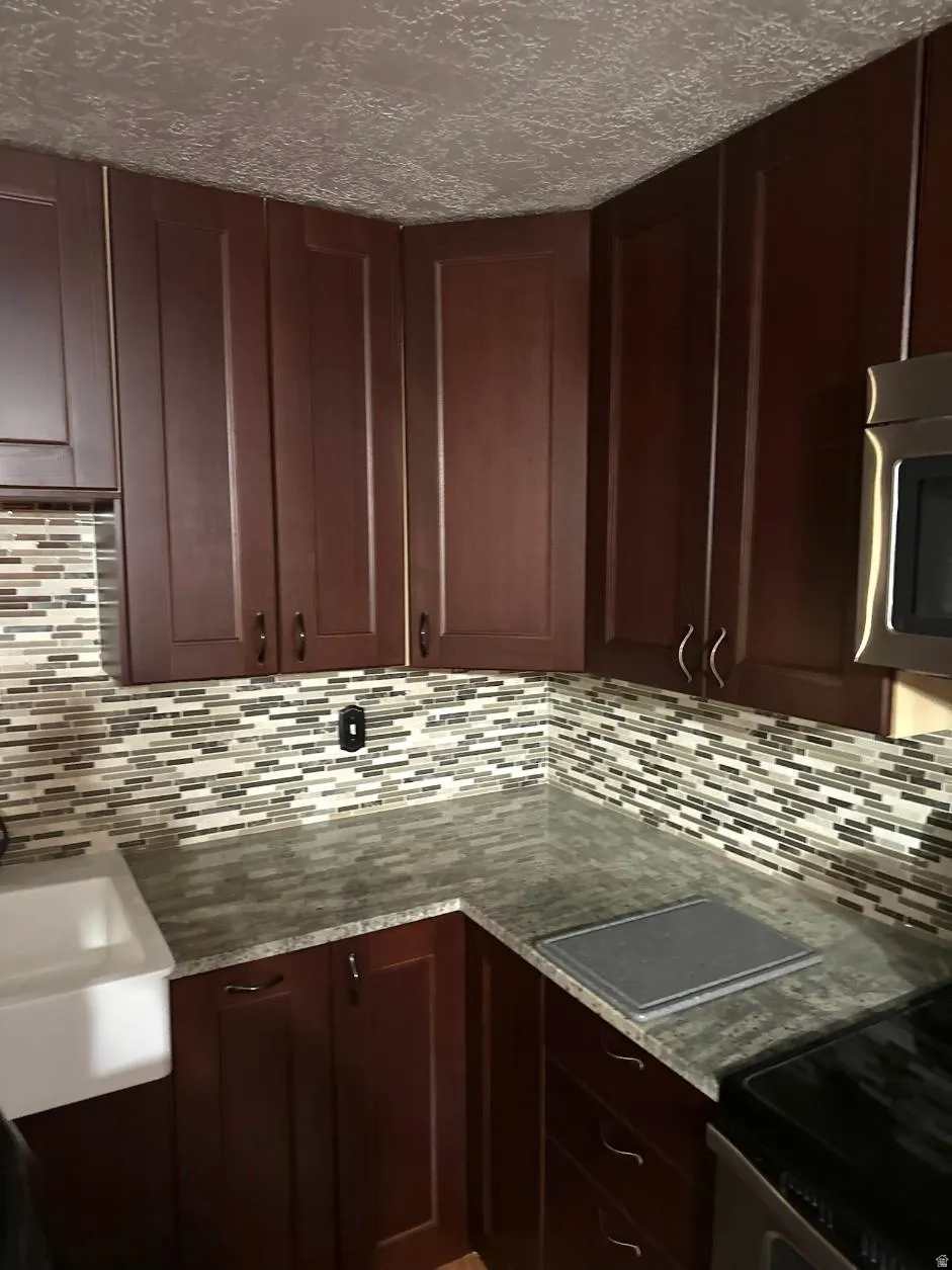 Dark wood-finish cabinetry, mosaic tile backsplash, stone-finish countertops, and an integrated farmhouse-style sink