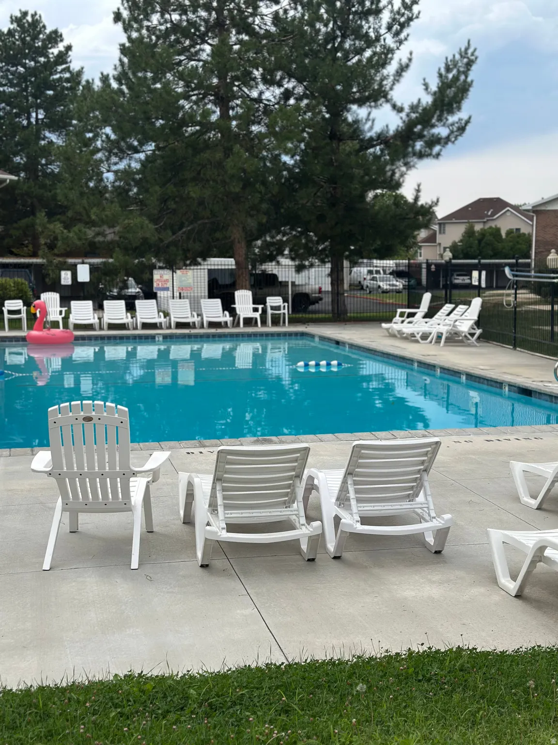 Outdoor swimming pool with a concrete surround, enclosed by a black metal fence