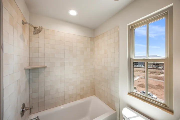 Bathtub with tile surround, built-in shower niche, chrome showerhead, and a double-pane window
