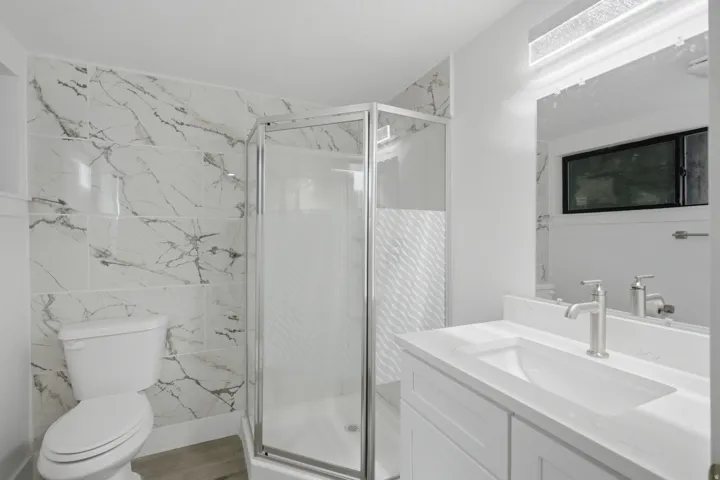 Corner shower with glass enclosure, marble surround, and brushed nickel fixtures