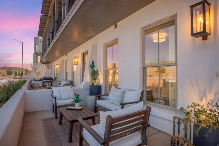 Patio featuring sconce lighting, white stucco walls, light gray window frames, and an upper-level balcony