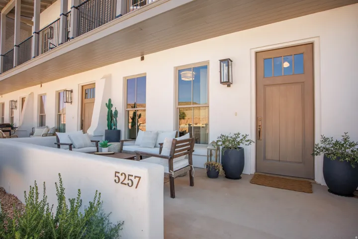 Private ground-level patio with stucco wall, wood-finish entry door with transom windows, and exterior wall lanterns