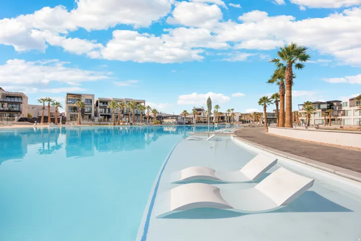 Expansive lagoon with integrated lounge chairs, bordered by a paved walkway and multiple palm trees
