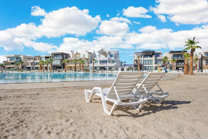 Sandy beach area with multiple lounge chairs, bordered by a large pool