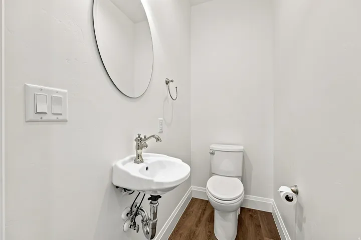 Pedestal sink with polished nickel faucet, oval mirror, white toilet, and wood-finish flooring