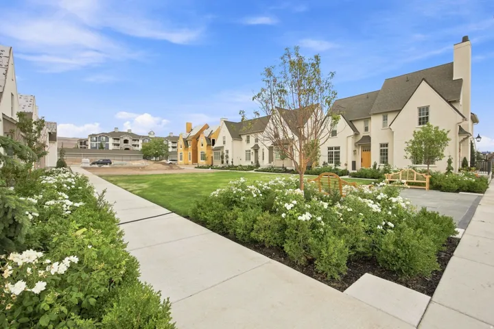 Manicured green space with mature plantings, paved walkway, and a landscaped garden bed featuring white flowering shrubs