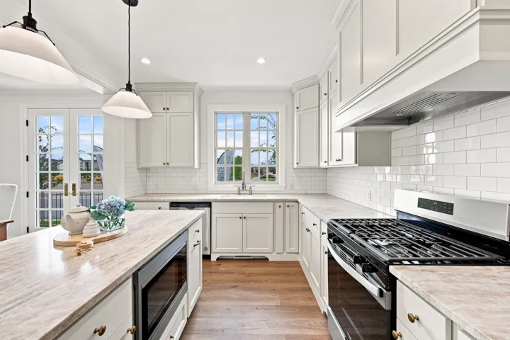 Kitchen featuring a built-in microwave, gas range, wood-finish flooring, white cabinetry, and a subway tile backsplash