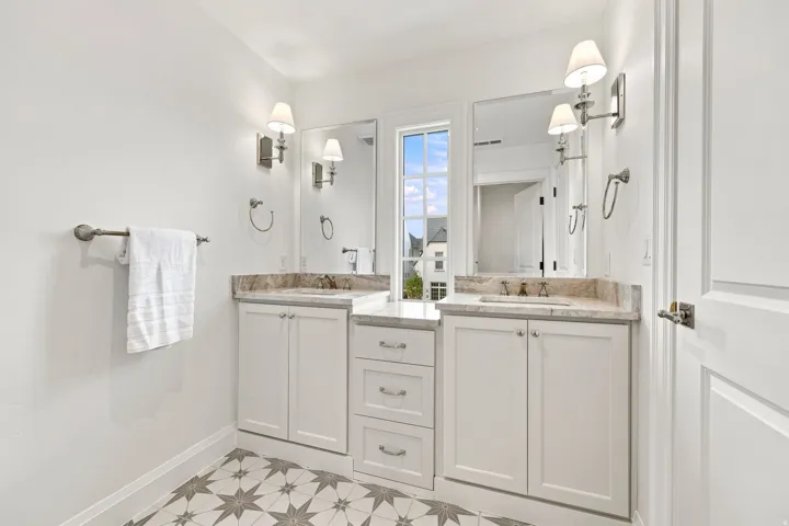 Dual vanity with stone countertops, white cabinetry, and patterned tile flooring