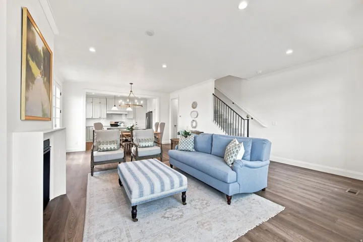 Hardwood-finish flooring throughout, recessed lighting, white fireplace mantel, open concept with kitchen beyond, and a staircase with black metal balusters