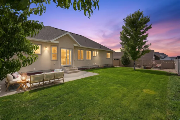 Expansive backyard featuring a manicured lawn, established shade tree, and a paved patio with steps leading to the residence
