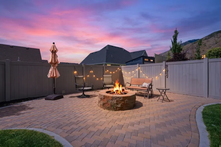 Paver patio with a stone fire pit, string lighting, and privacy fencing