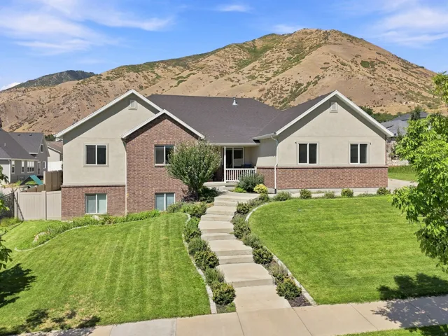 Two-story residence featuring brick and stucco exterior, prominent gabled rooflines, and a concrete pathway with integrated landscaping