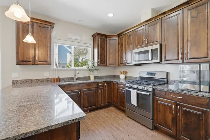 Wood-finish flooring, stainless steel appliances, dark wood cabinetry, granite countertops, and a stainless steel sink with a high-arc faucet