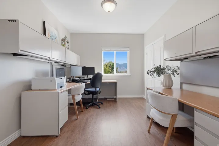 Dedicated workspace with wood-finish flooring, built-in cabinetry, and a window providing natural light